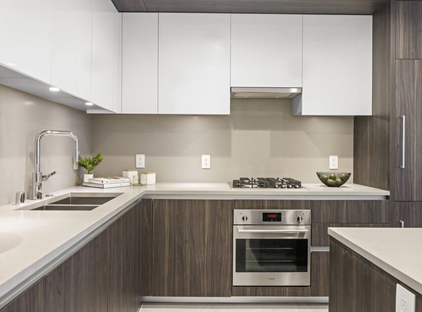 Modern kitchen with white upper cabinets, dark wood lower cabinets, stainless steel oven, built-in gas cooktop, sink with a tall faucet, and a bowl of green apples on the counter. Bright, clean, and minimalistic design.