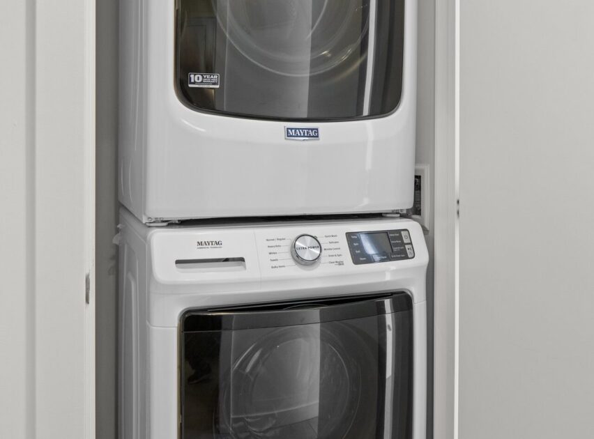 A stacked white Maytag washer and dryer set fitted in a narrow laundry closet with the dryer on top and the washer below, both with front-loading doors.
