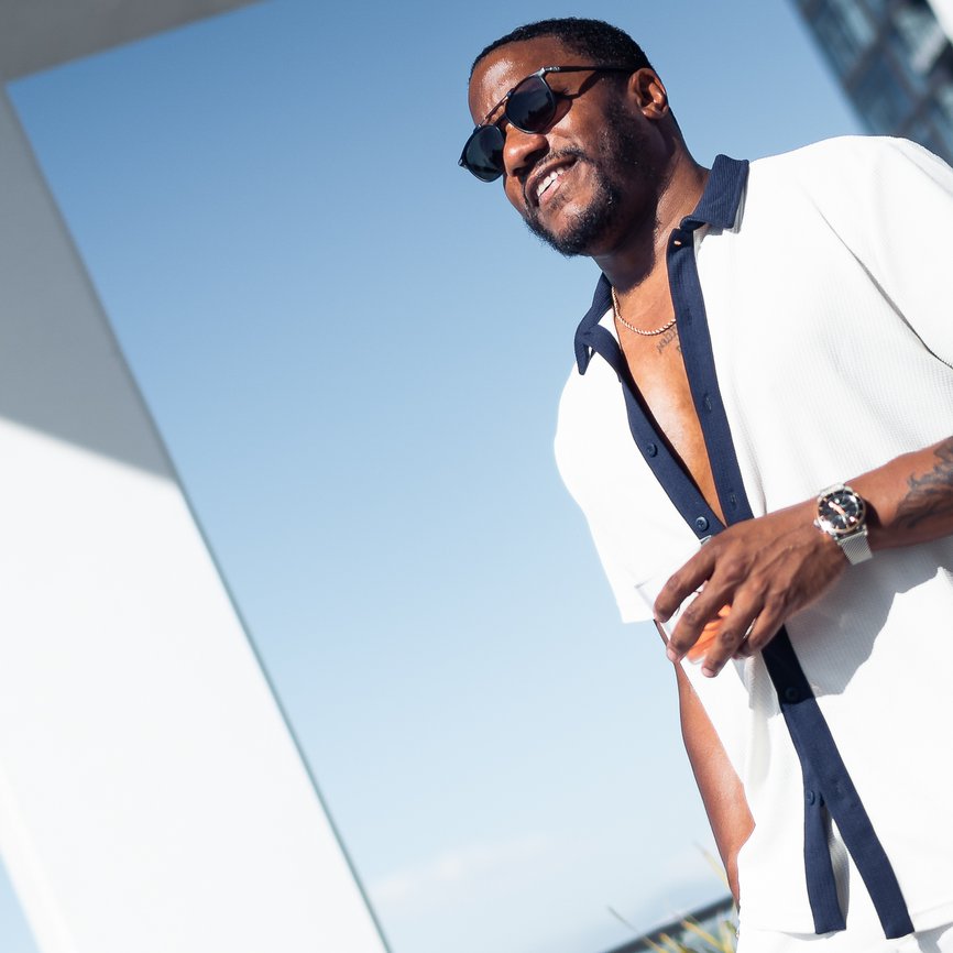 man standing outside in the sun on balcony with a drink in hand