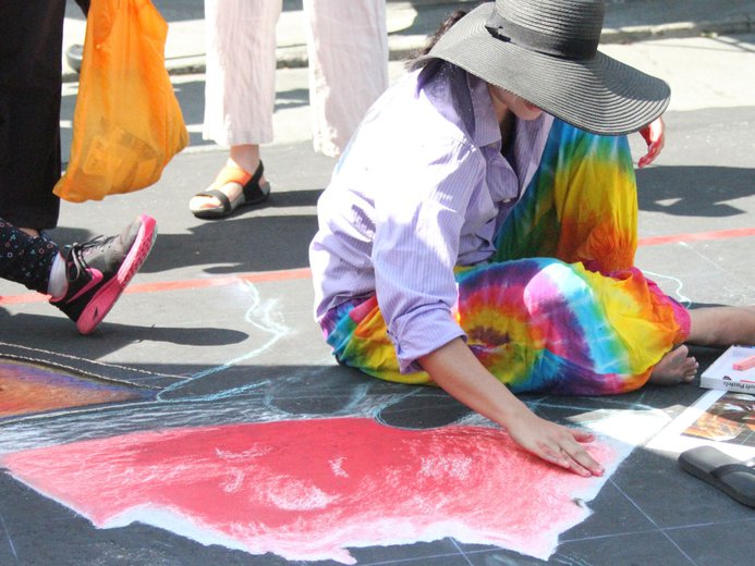 Lady in sunhat at Port Moody Arts Festival painting the ground pink with chalk in her hands