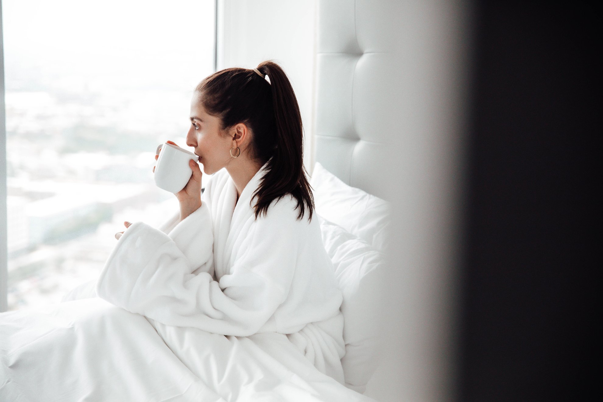a girl in bathroom sipping coffee on bed