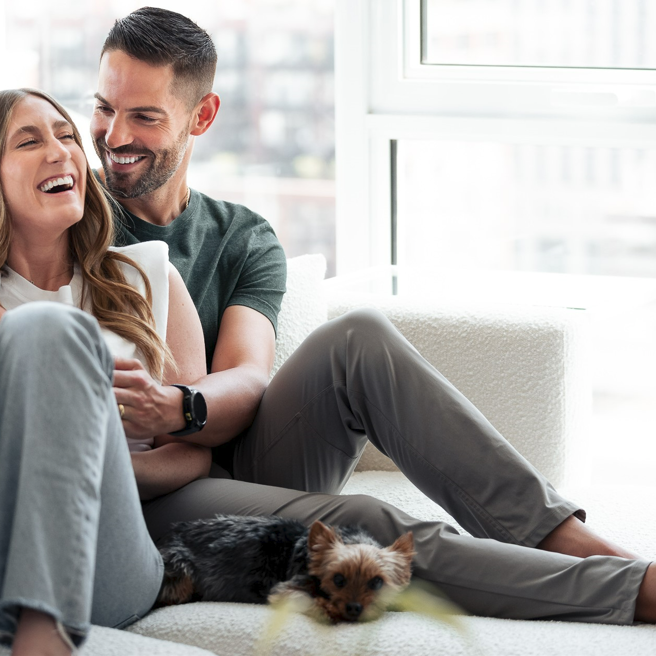 couple sitting on couch laughing together with their little dog