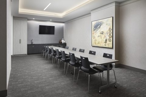 A modern, empty conference room with a long rectangular table, ten black chairs, a mounted flat-screen TV, abstract wall art, and cabinets along the back wall under soft ceiling lighting.