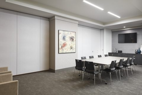 Modern conference room with a rectangular table, black chairs, abstract art on the wall, a flat-screen TV, and a cabinet with decorative vases under bright ceiling lights.