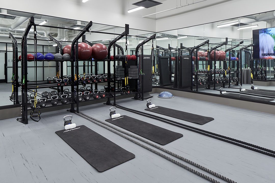 A modern gym with exercise mats, kettlebells, battle ropes, stability balls, and various weights arranged neatly in front of large mirrors on the wall.