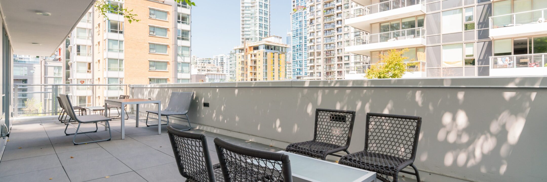 Spacious outdoor patio with modern black chairs and tables, surrounded by tall apartment buildings with balconies, under a clear sky.