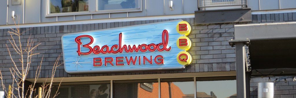 A sign for Beachwood Brewing BBQ with retro-style red and yellow lettering is mounted on the exterior of a gray brick building.